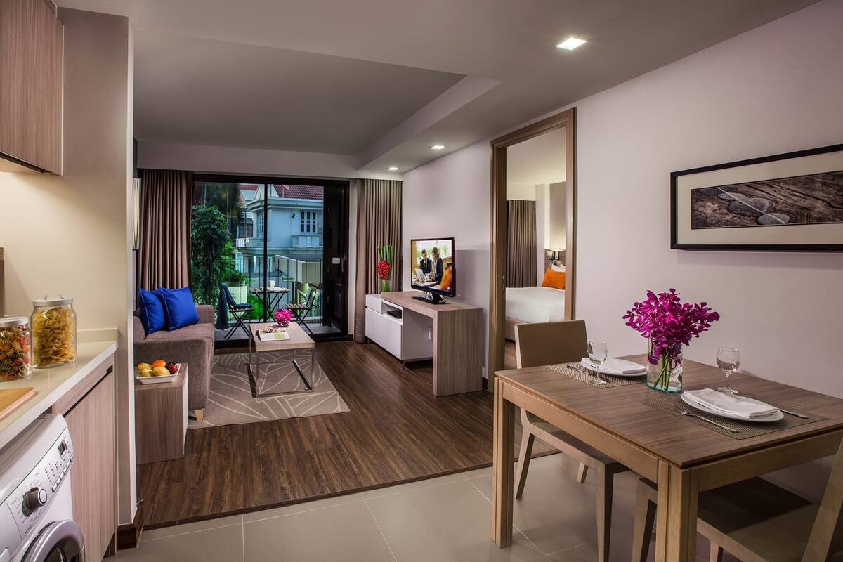 A modern hotel room with a dining area, a sofa, a TV, and a view of the outside.