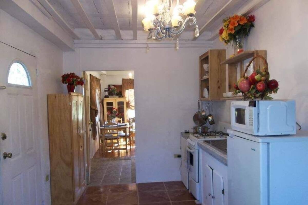 Un couloir étroit mène à une cuisine équipée d’une cuisinière, d’un four à micro-ondes et de placards. Une porte en bois se trouve à gauche et une fenêtre à droite.