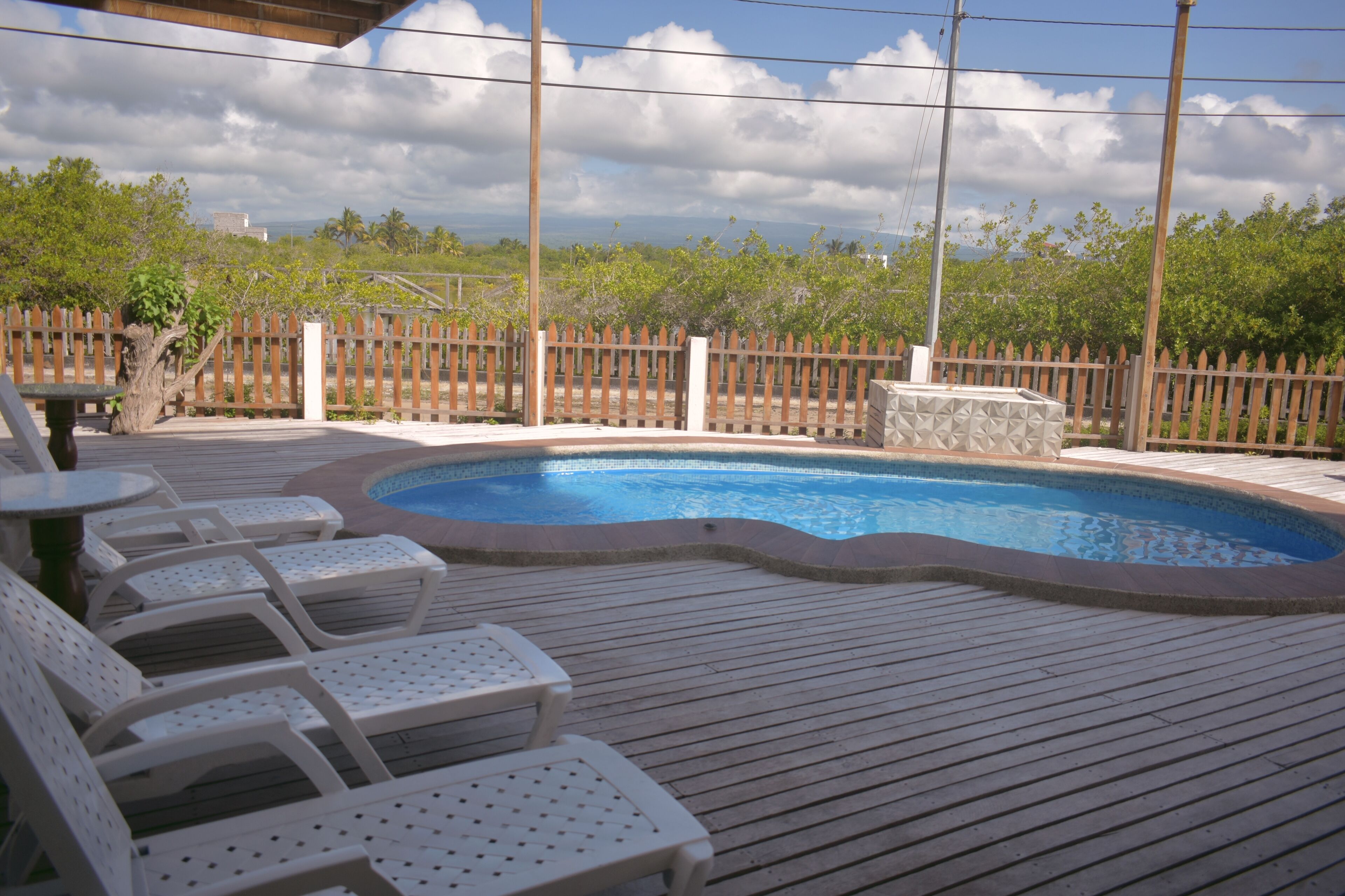 A wooden deck with a swimming pool, white lounge chairs, and a wooden fence.