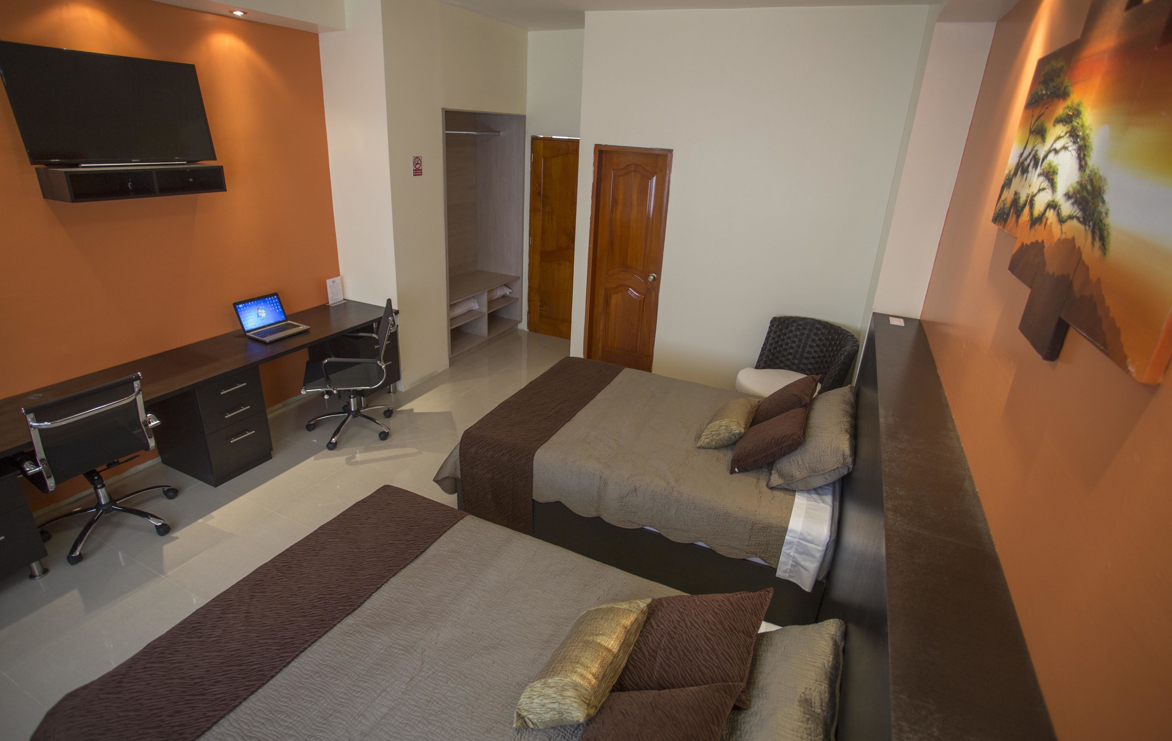 Habitación de hotel con dos camas, un escritorio con una computadora portátil, una silla y un armario.