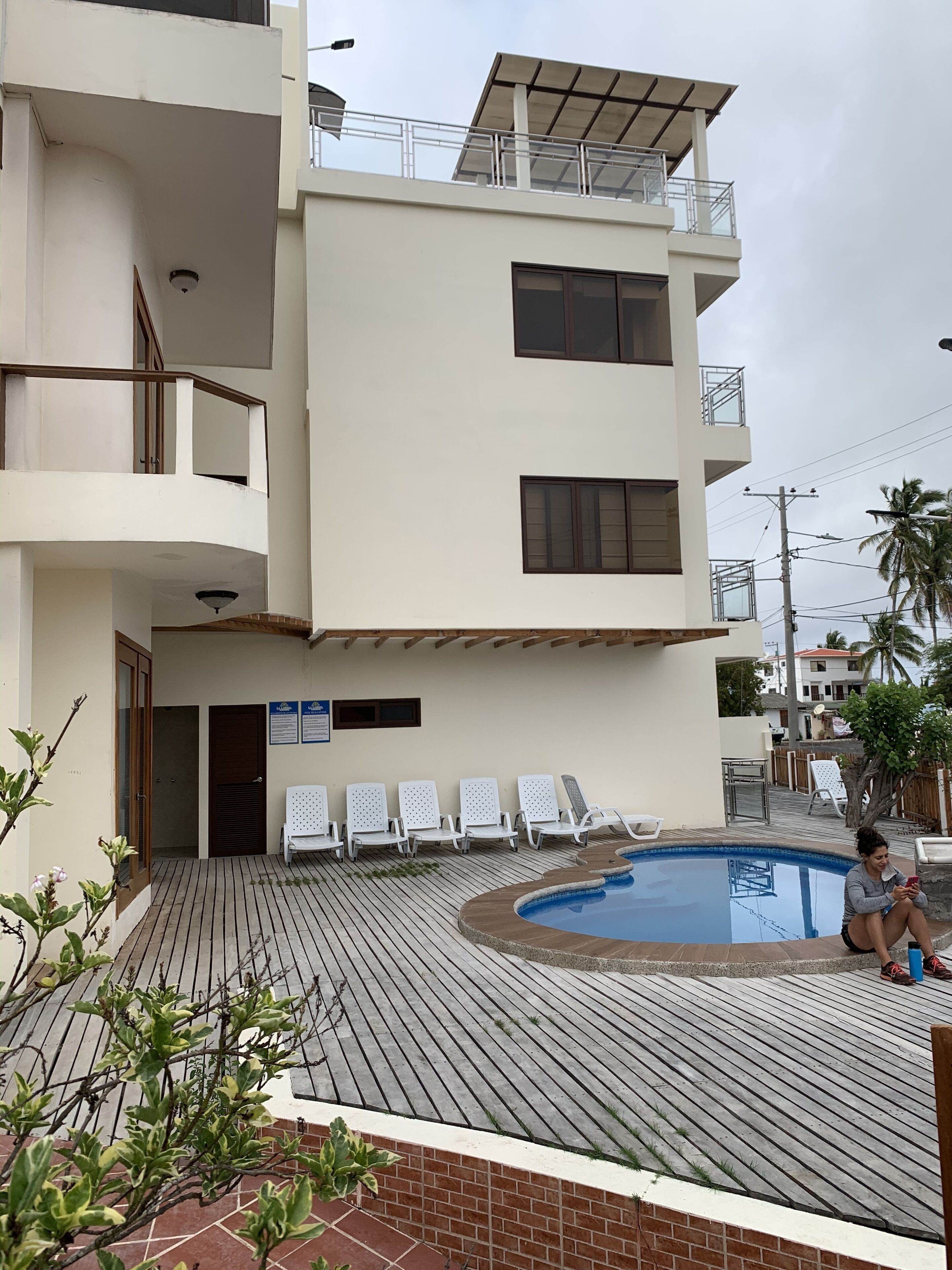 Un bâtiment moderne doté d’une piscine, de chaises longues blanches et d’une terrasse en bois.