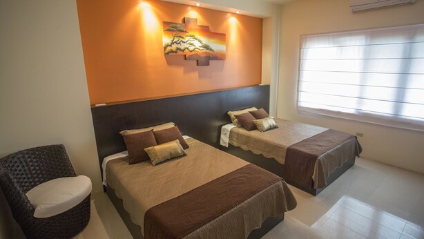 Une chambre d’hôtel avec deux lits, une chaise, un tableau au mur et une fenêtre avec des stores.