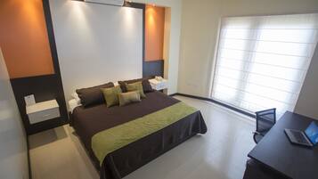 A modern hotel room with a large bed, bedside table, and a desk with a laptop.