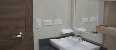 A bathroom with a wooden door, a white sink, a mirror, and a shelf with towels.