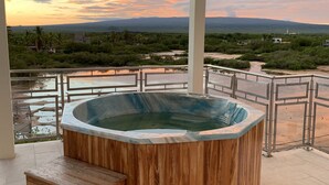 Un bain à remous avec des marches en bois et une vue sur un paysage verdoyant, avec des montagnes à l’horizon.