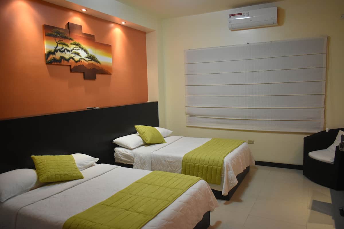 Habitació d'hotel amb dos llits, cadascun amb llençols blancs i una manta verda. Hi ha un quadre a la paret i una finestra gran amb persianes.