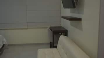 A room with a white sofa, a small table, a mounted TV, and an air conditioning unit.