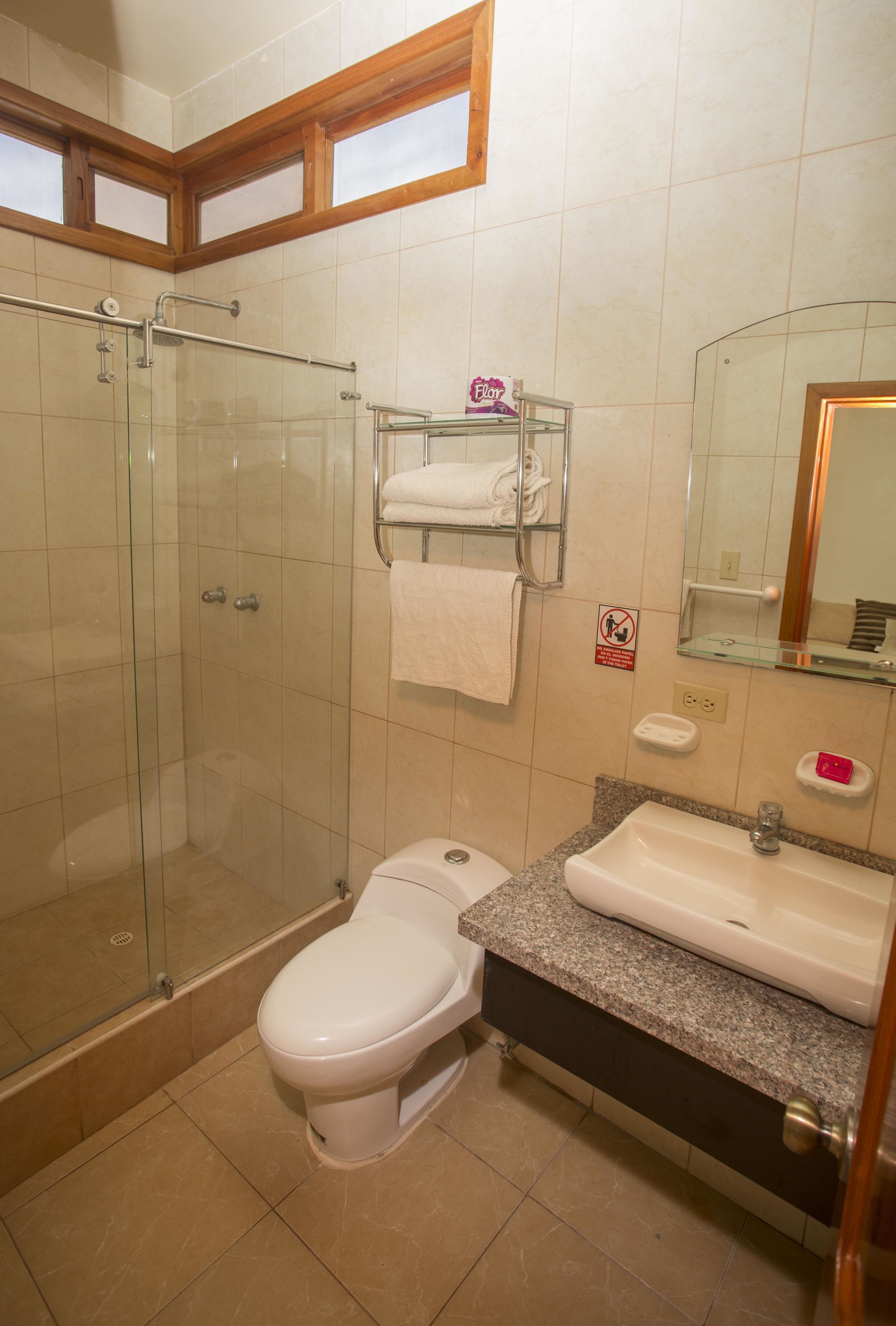 Un baño con ducha de vidrio, inodoro, lavamanos y barra para toallas.