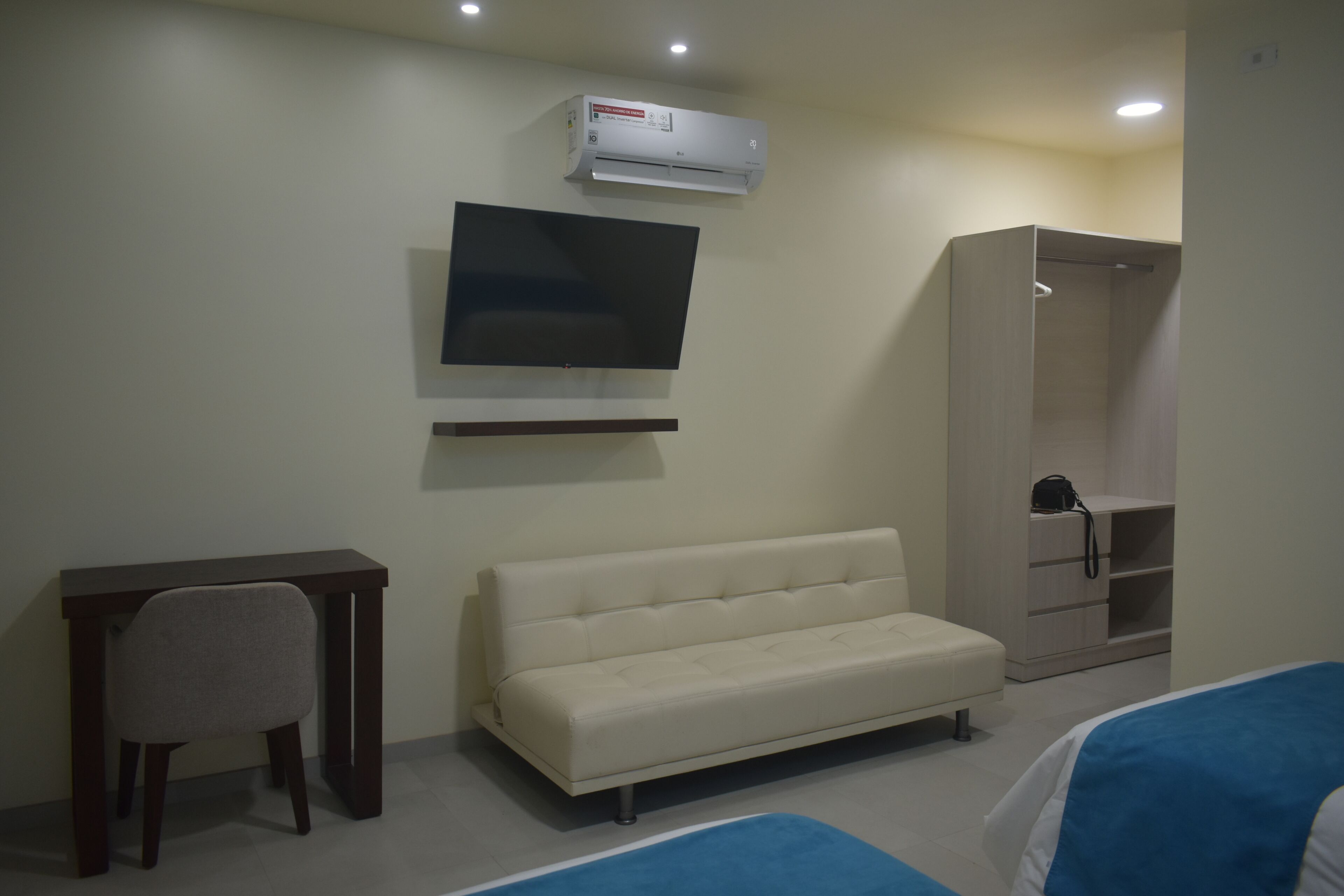 Habitación de hotel con sofá, televisor montado en la pared, escritorio y armario.