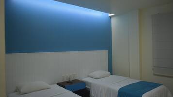 Habitación de hotel con dos camas, una mesita de noche y una pared azul de acento.