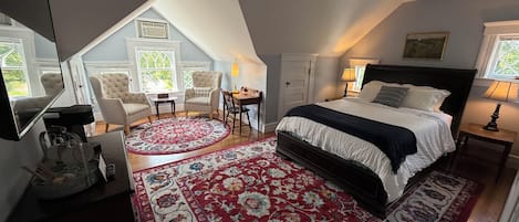 Une chambre à coucher avec un grand lit, deux chaises, une petite table et un tapis rouge à motifs.