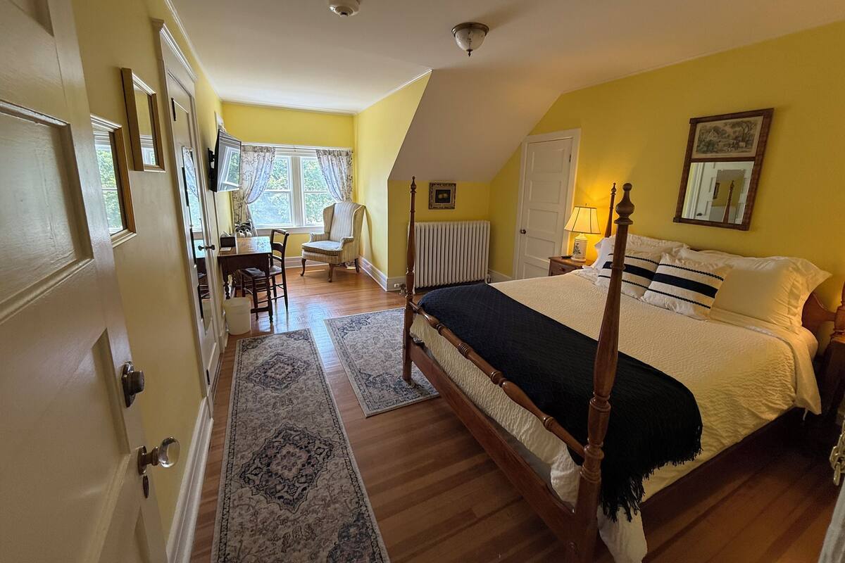 A bedroom with a four-poster bed, a desk, and a chair.