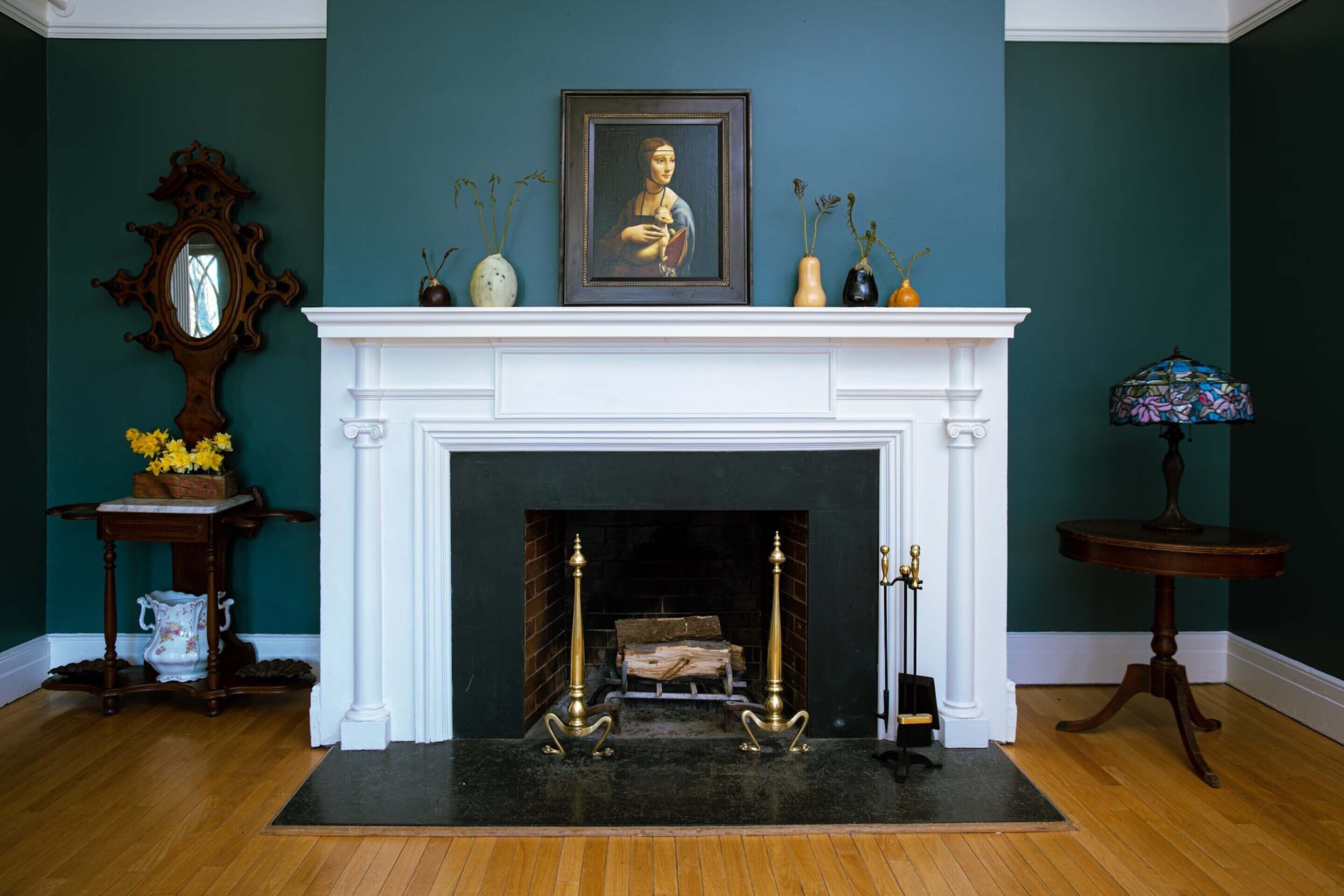 A room with a white fireplace, a framed painting above it, and a vase with flowers on a side table.