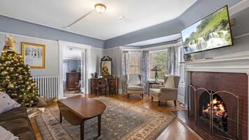 A living room with a fireplace, a television, a Christmas tree, and a dining area.