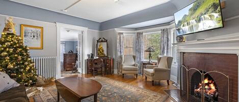 A living room with a fireplace, a television, a Christmas tree, and a dining area.