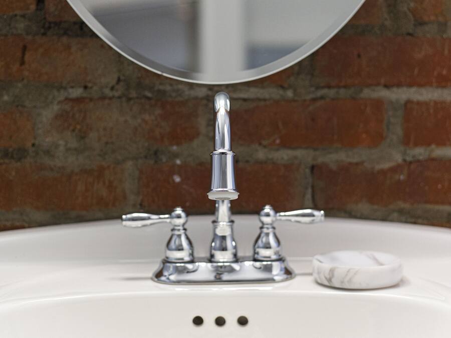 A white bathroom sink with a chrome faucet and a round mirror above it.