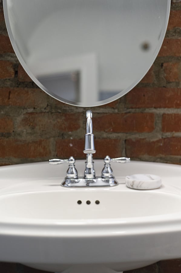 A white bathroom sink with a chrome faucet and a round mirror above it.
