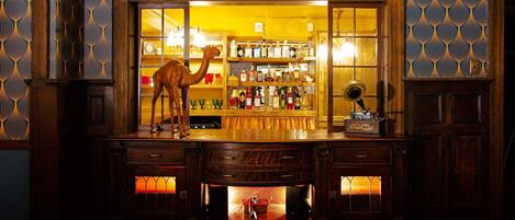 A bar area with a wooden counter, shelves of bottles, and a decorative camel statue.