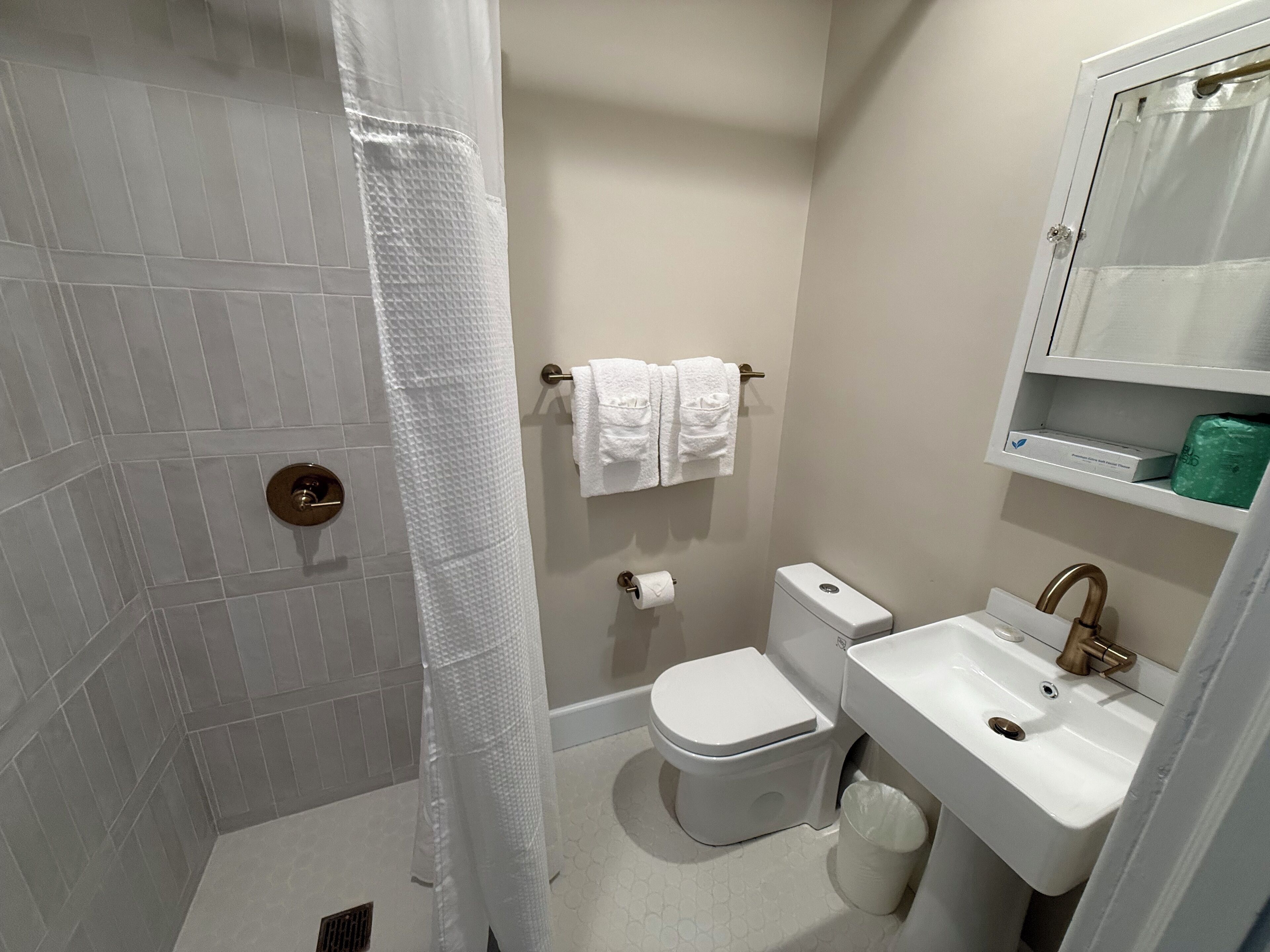 A bathroom with a shower, toilet, sink, and towel rack.