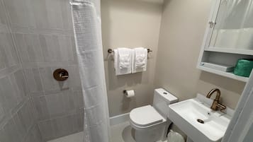 A bathroom with a shower, toilet, sink, and towel rack.