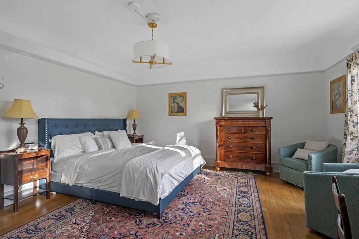 A bedroom with a large bed, a dresser, a chair, and a ceiling fan.