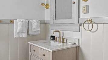 Une salle de bain avec un meuble-lavabo blanc, un miroir, un évier et des toilettes. Des serviettes sont accrochées au mur et un luminaire est fixé au-dessus du miroir.