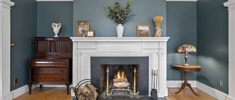 A room with a fireplace, a wooden dresser, a vase with flowers, and a small table with a lamp.