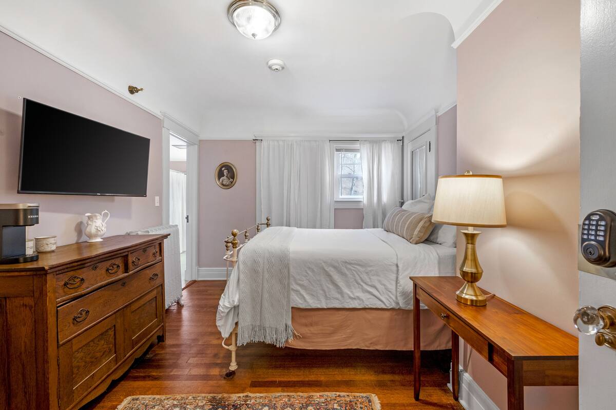 A bedroom with a bed, a dresser, a television, a lamp, and a door with a keypad lock.