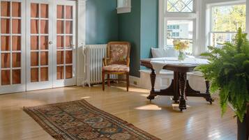A room with a patterned rug, a wooden chair, a table with a vase, and a large plant.