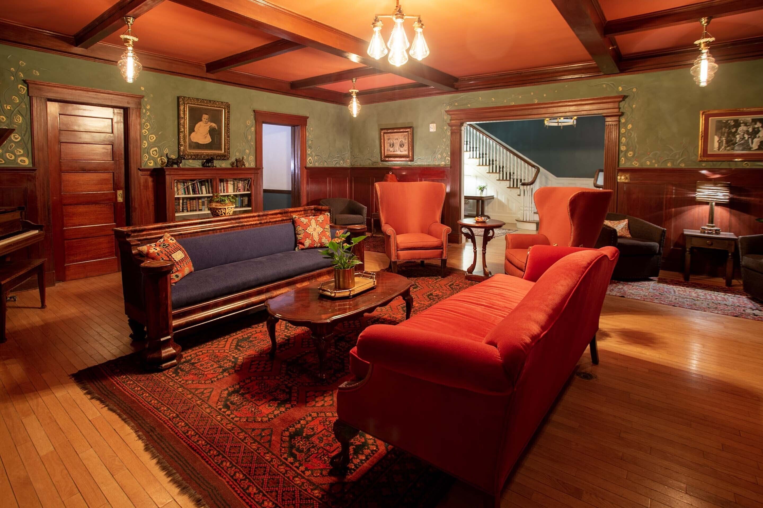 A traditional living room with a wooden floor, a red sofa, a blue sofa, a wooden coffee table, and a staircase in the background.