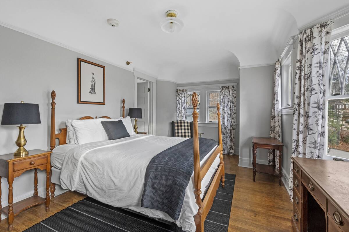 A bedroom with a large bed, two bedside tables, a dresser, a framed picture on the wall, and a window with curtains.