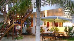 A beachside patio with a wooden staircase, a palm tree, and a covered seating area with a table and chairs. - Hotel San Vicente Galapagos (Puerto Villamil)