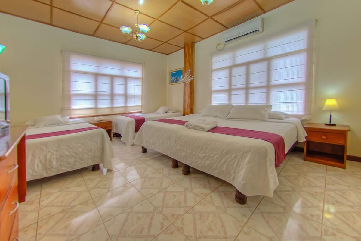 Habitación de hotel con tres camas, techo de madera y ventanas grandes con persianas.