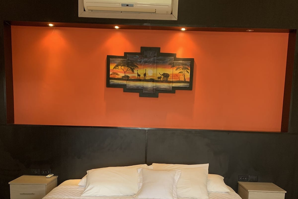 Habitación de hotel con una cama grande, dos mesitas de noche, un aire acondicionado de pared y un cuadro enmarcado sobre la cama.