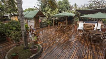 A wooden deck with outdoor seating, surrounded by potted plants and a small pool area.