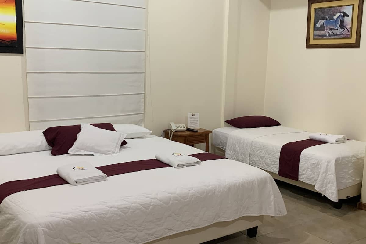 Habitación de hotel con dos camas, cada una con ropa de cama blanca y almohadas color burdeos.  Se ve una mesita de noche con un teléfono y un cuadro en la pared.