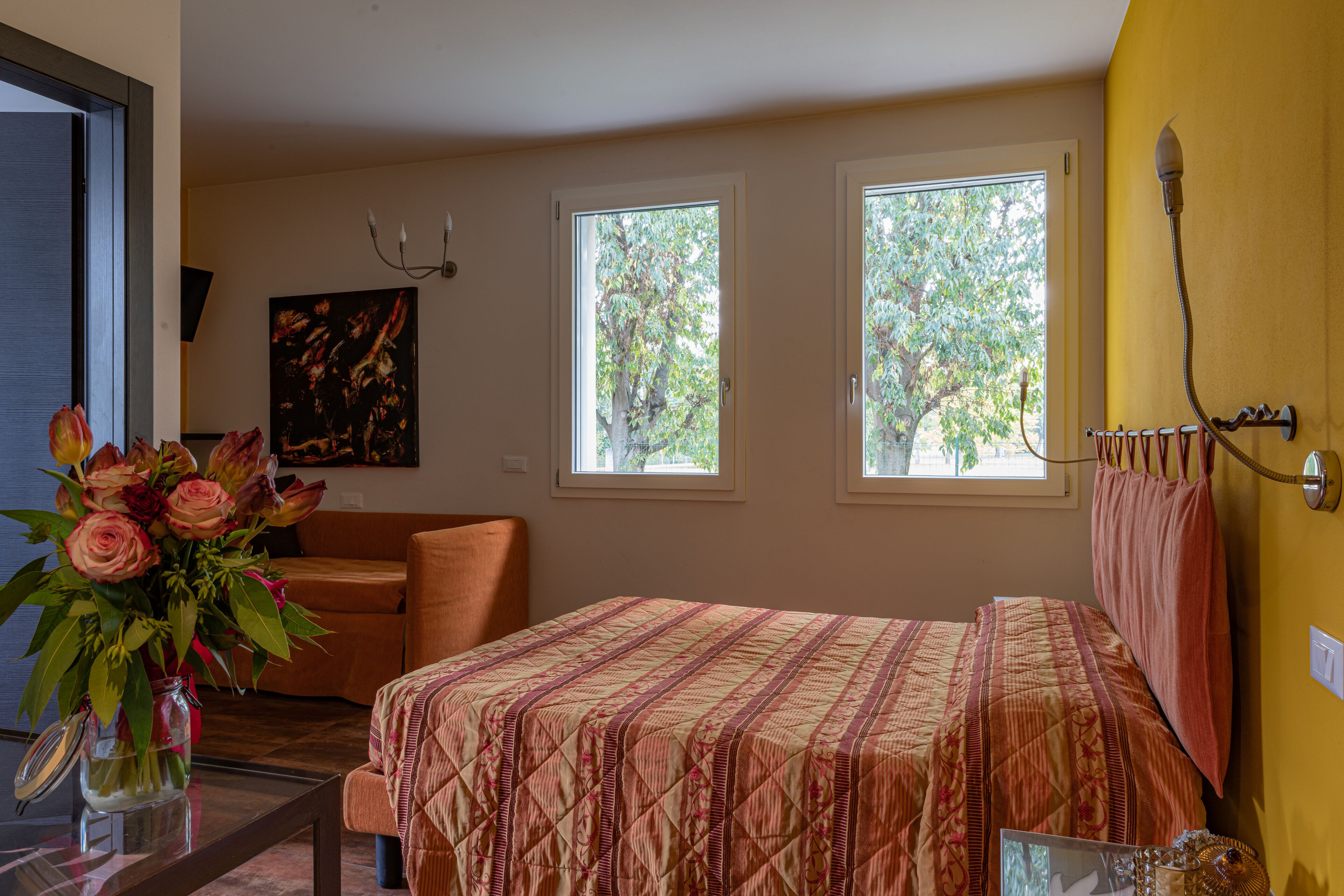 Une chambre à coucher avec un lit, une fenêtre, un vase de fleurs et un tableau accroché au mur.