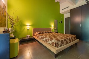 A modern bedroom with a green wall, a bed with a patterned bedspread, a bedside table with a lamp, and a large wardrobe.