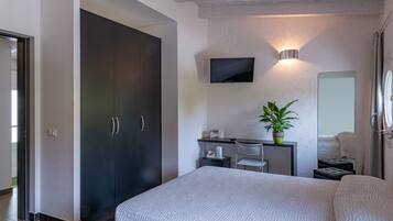 Une chambre à coucher moderne avec un grand lit, une armoire sombre, un bureau avec une chaise, un téléviseur à écran plat, une plante en pot et un miroir.