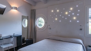 Ein Schlafzimmer mit einem Bett, einem Schreibtisch mit Stuhl, einem runden Fenster und einer Wand mit sternförmigen Lichtern.