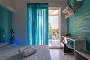 A hotel room with a bed, a desk, a chair, a TV, and a sliding glass door leading to a balcony.