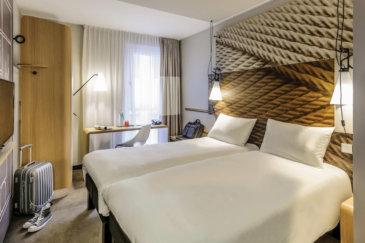 Et hotelværelse med seng, skrivebord, stol, kuffert og fjernsyn.