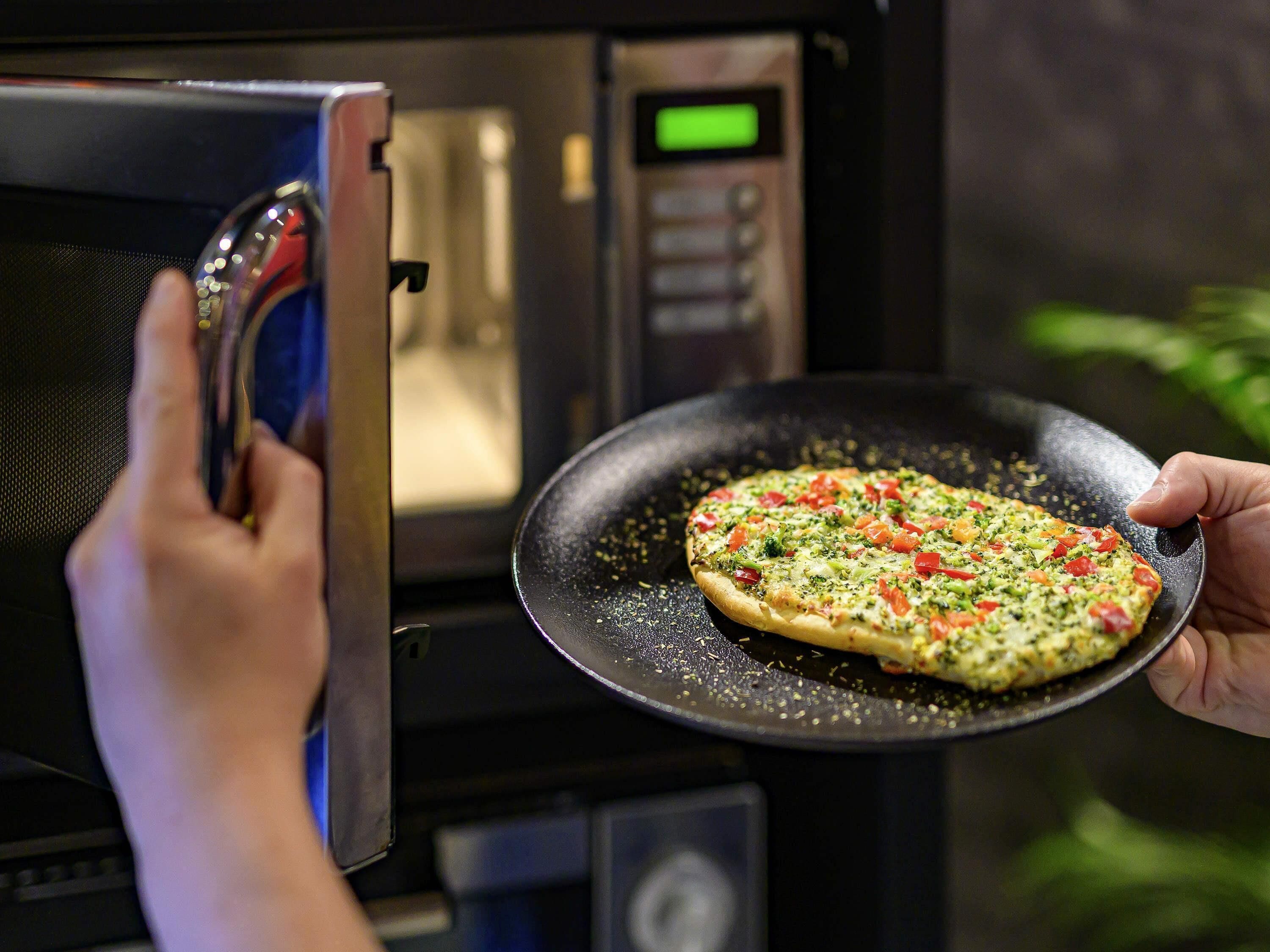 Una persona sosteniendo una pizza dentro de un microondas.