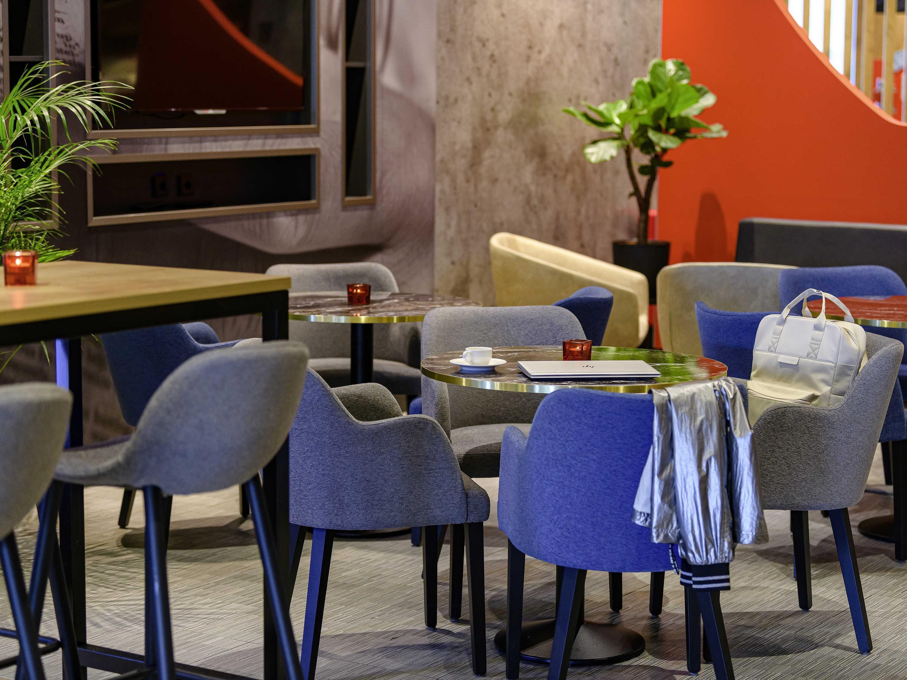 Ein modernes Café-Interieur mit runden Tischen, grau gepolsterten Stühlen und einem Blumentopf.