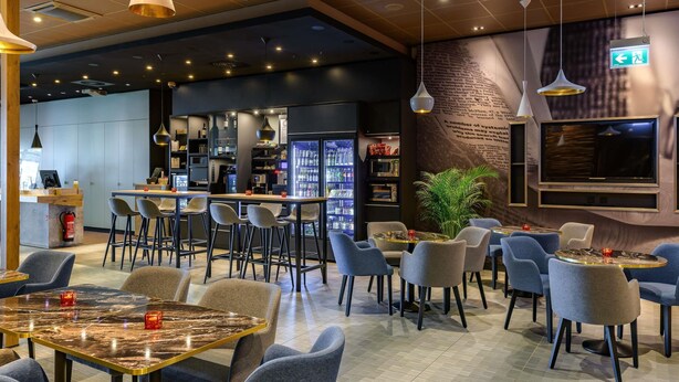 Un interior de restaurante moderno con asientos de bar, una barra y una pantalla de televisión.