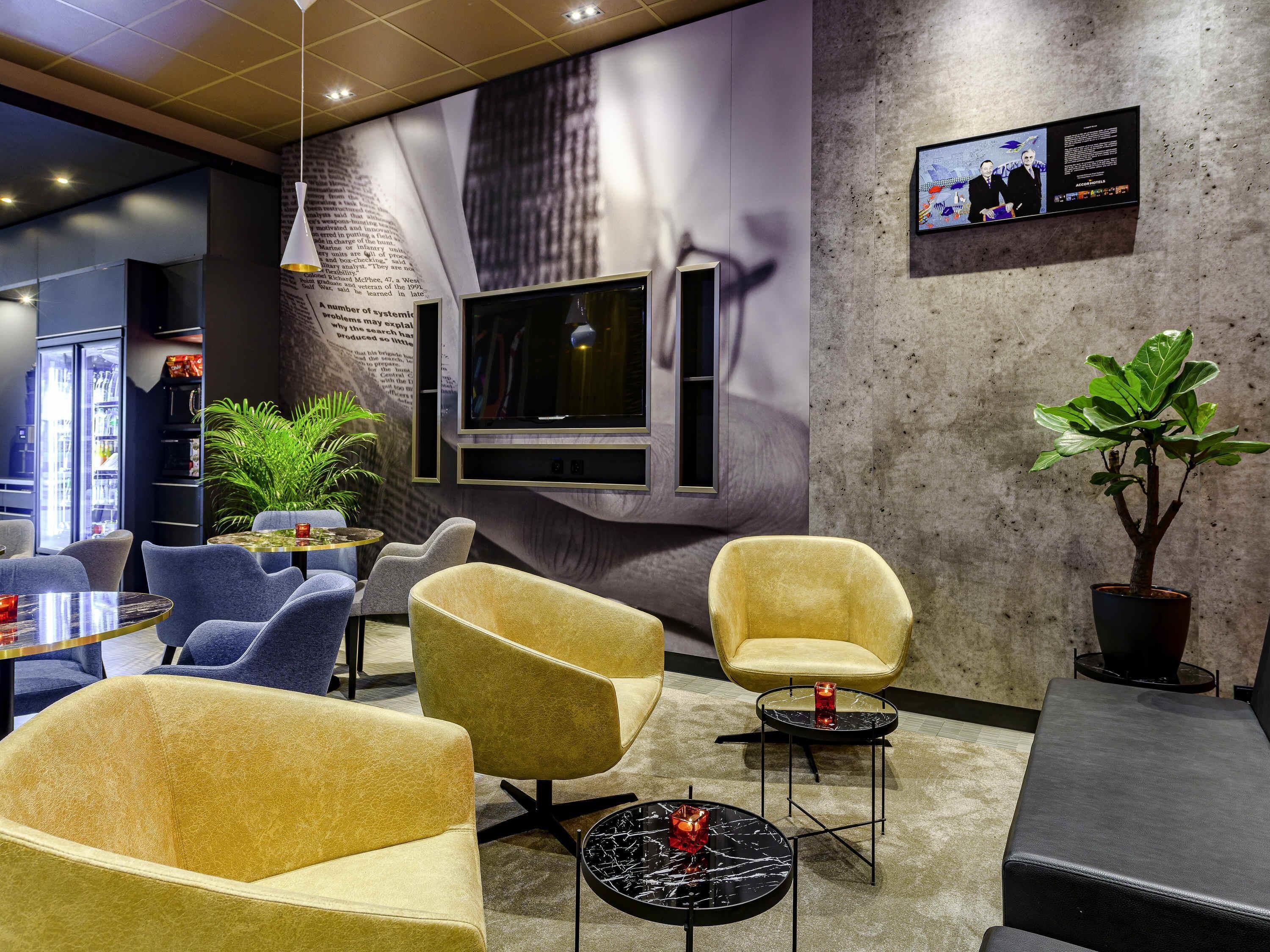 A modern lounge area with comfortable seating, a television, and a large wall mural.