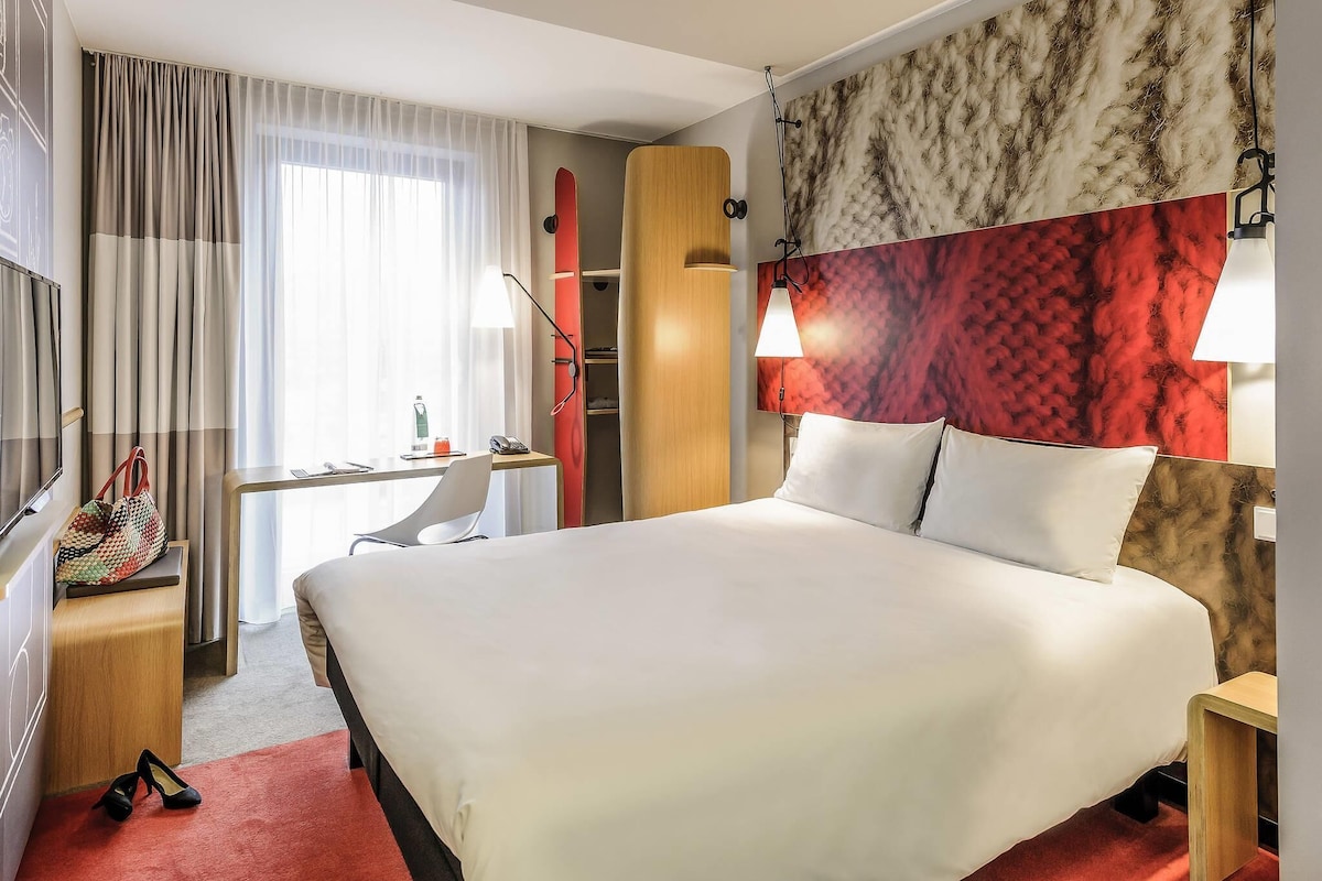 Et hotelværelse med seng, skrivebord, skab og fjernsyn.