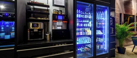 A minibar with a digital coffee maker, a refrigerator stocked with beverages, and a potted plant.