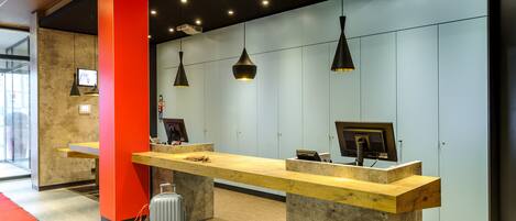 A reception desk with a wooden counter, a red pillar, and a grey suitcase.