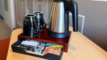 A coffee maker, two mugs, and a tray with coffee pods and a tea bag on a wooden table.